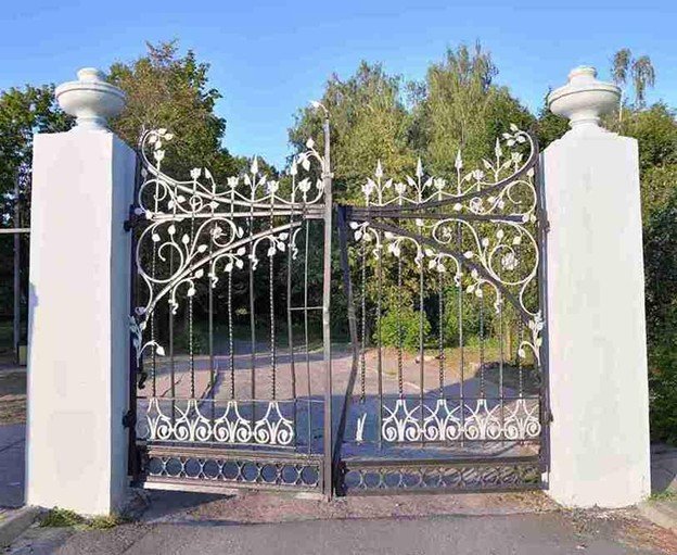 Decorative wrought iron driveway gate installed between two white columns at a residential entrance.