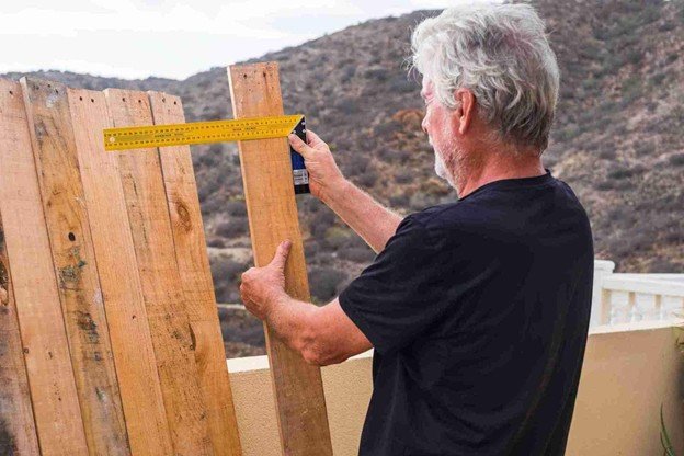 Contractor measuring and aligning cedar boards during a board-on-board fence installation for proper spacing and straight layout.