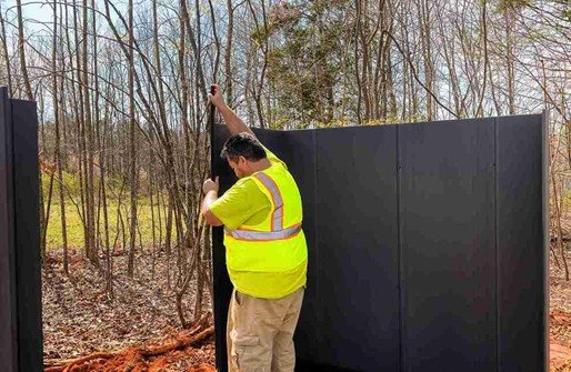 Worker installing a tall privacy fence panel outdoors wearing safety gear