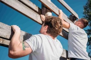 Two workers installing a cedar wood fence under a clear blue sky