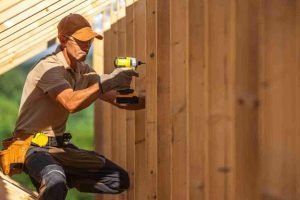 Fence contractor installing cedar fence boards using power tools on a residential property